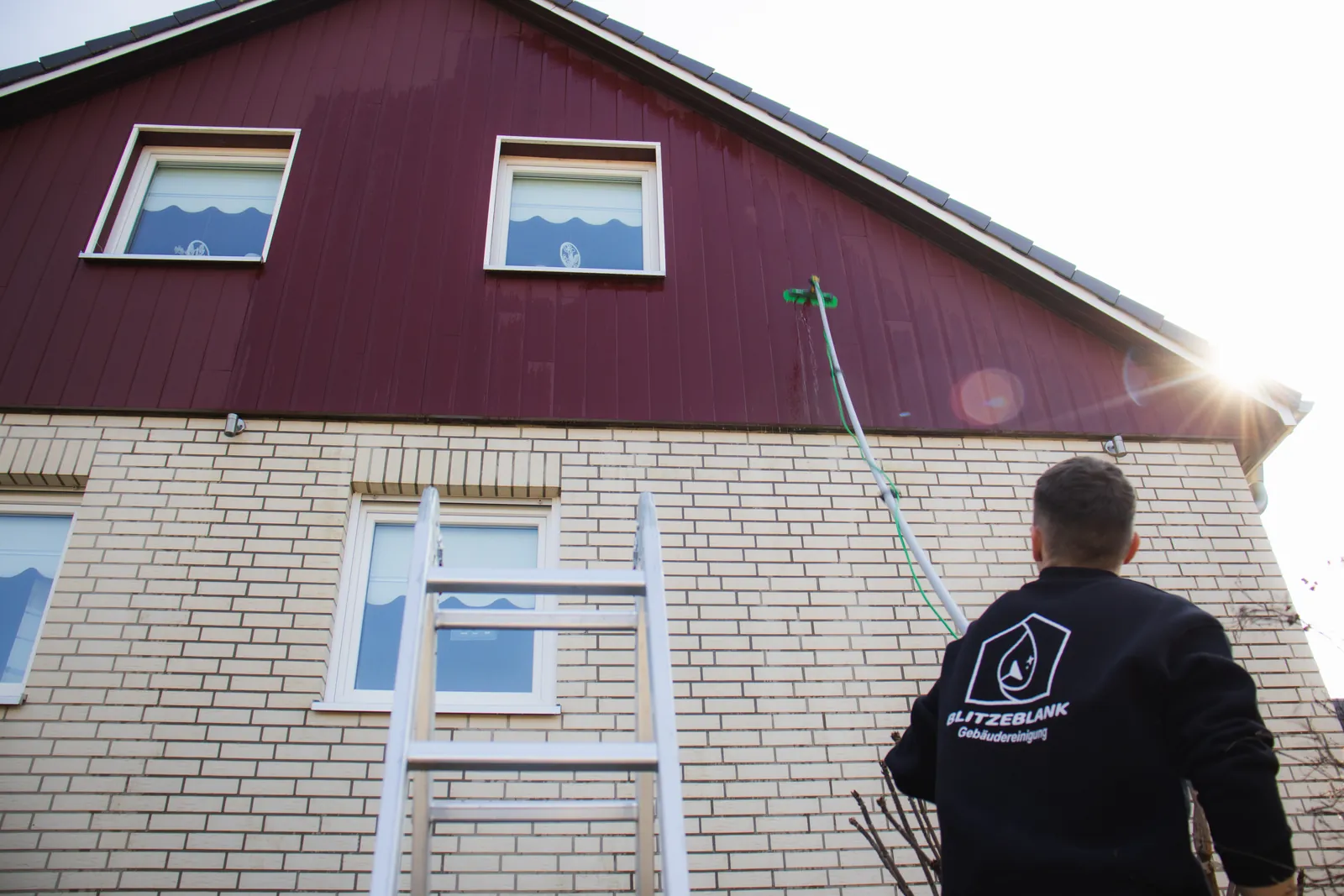 Fensterreinigung an einem Einfamilienhaus in Lübeck – BlitzeBlank Mitarbeiter reinigt die Giebelfenster mit Teleskopstange vom Boden aus