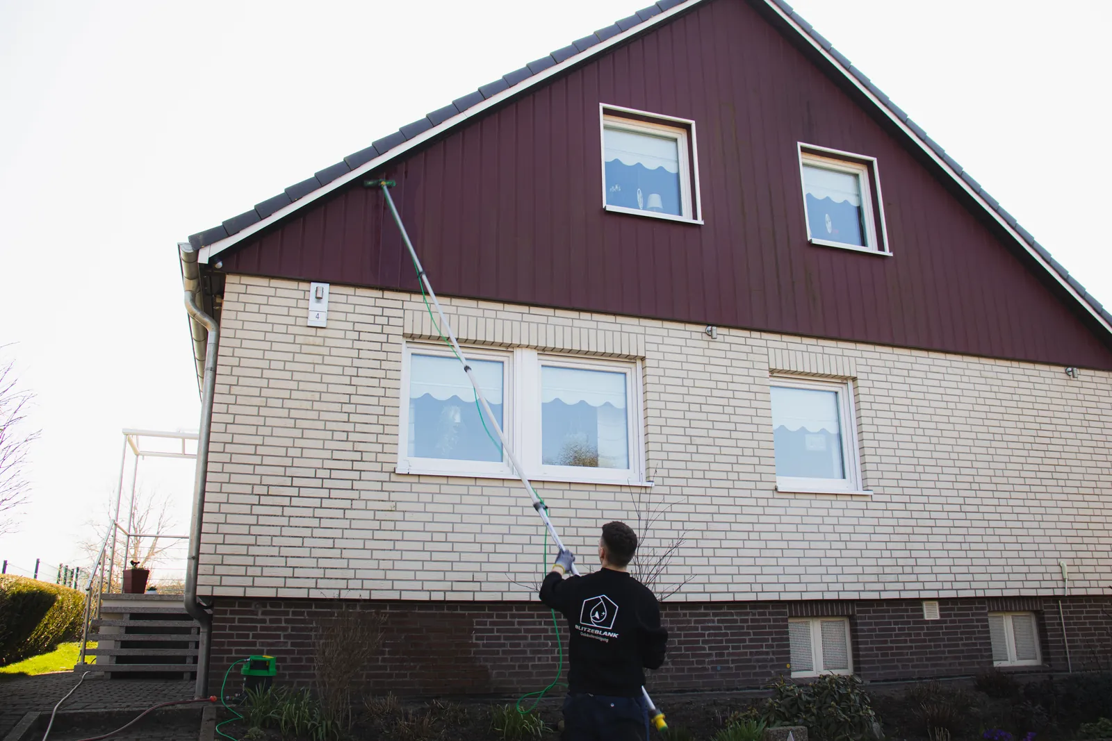 Hausmeisterservice in Lübeck – BlitzeBlank Mitarbeiter reinigt die Fenster eines Einfamilienhauses mit Teleskopstange